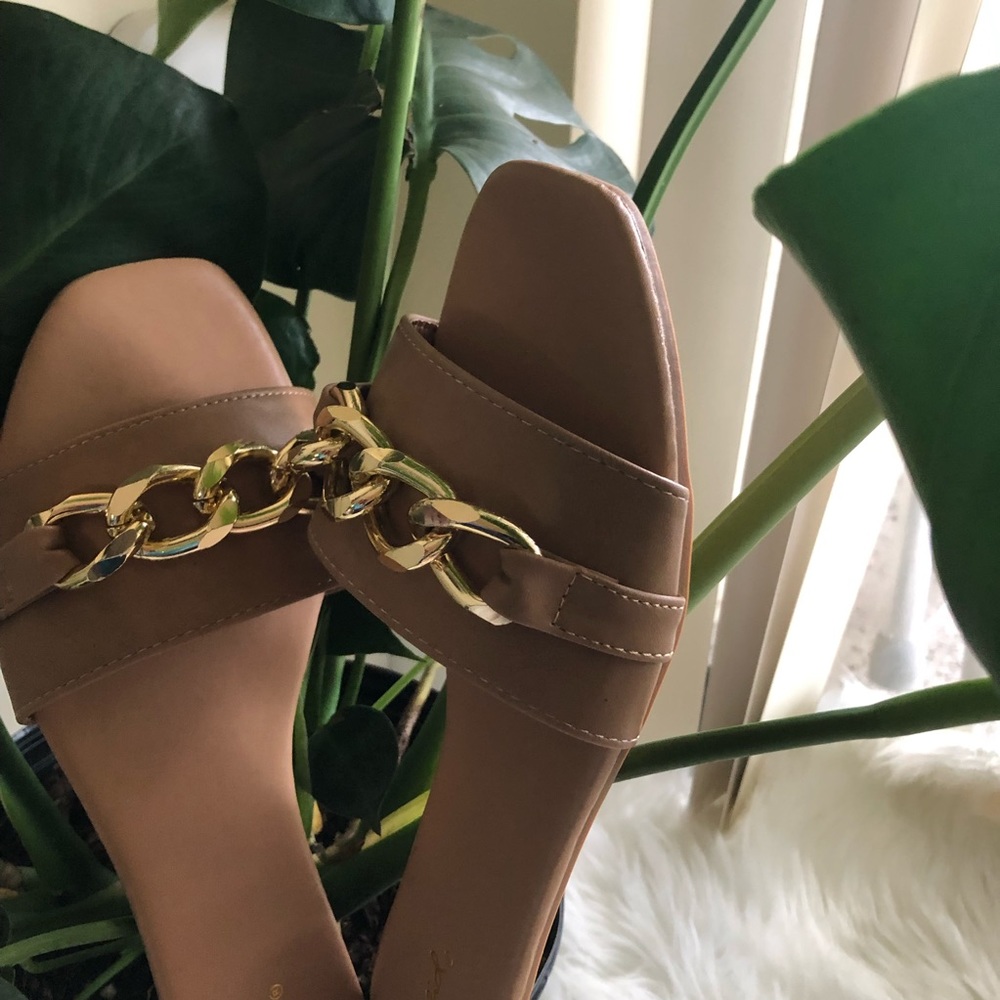 Neutral flat sandals with gold chain on top.